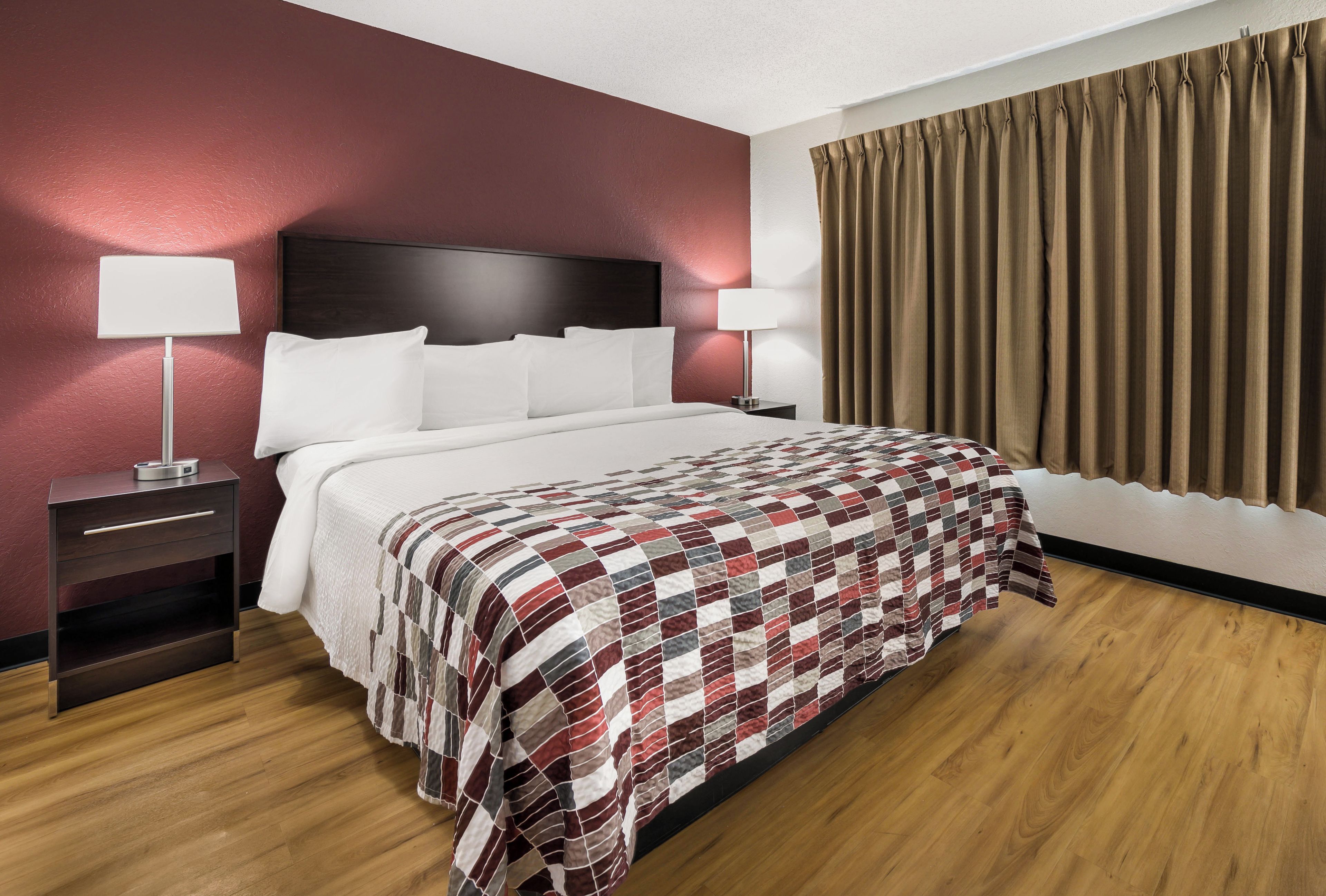 Habitación de hotel con una cama grande, dos mesitas de noche, un cabecero y un ventanal con cortinas.