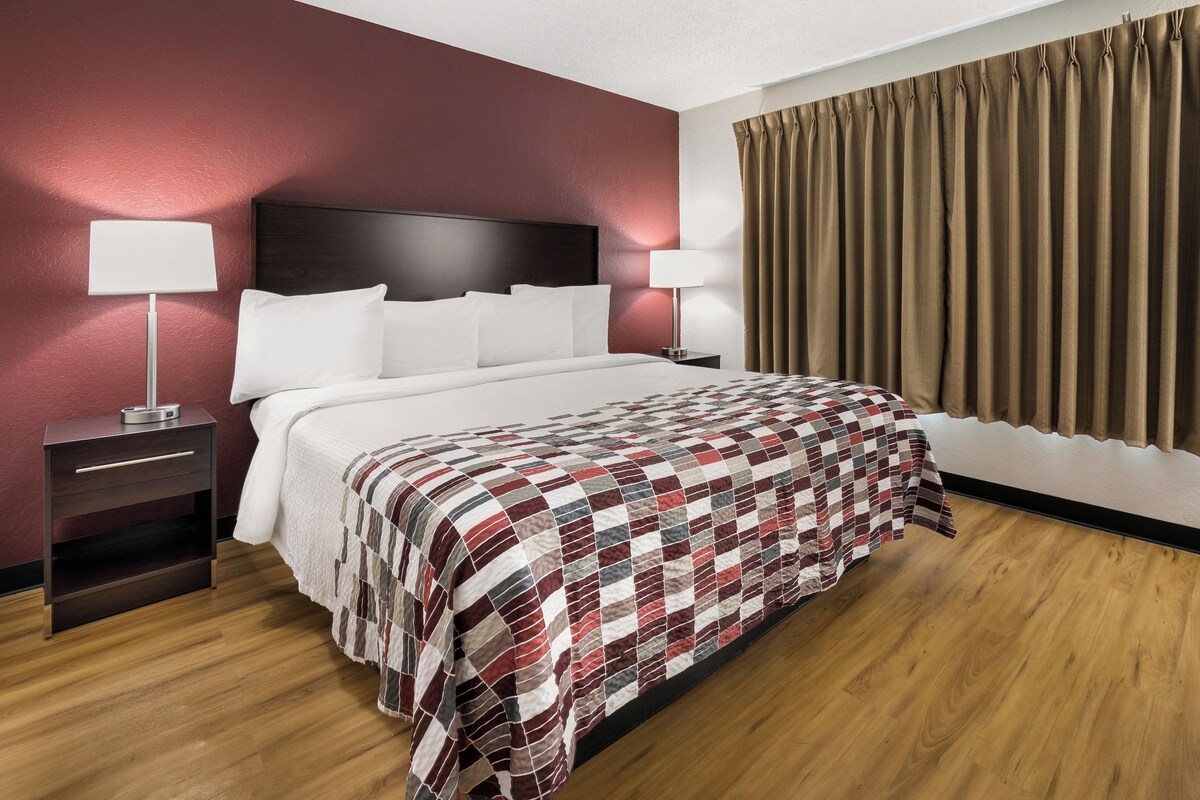 A hotel room with a large bed, two bedside tables, a headboard, and a window with curtains.