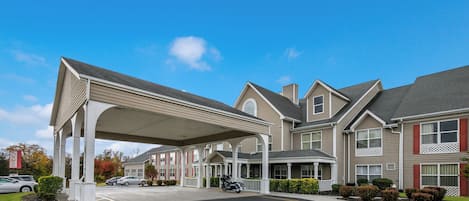 A large hotel with a covered entrance, multiple windows, and a parking lot.