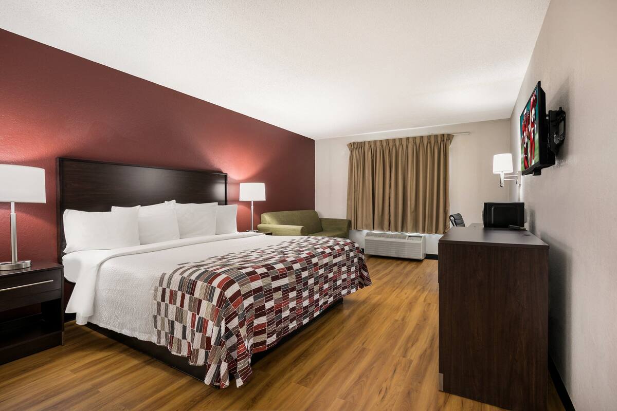 Une chambre d’hôtel avec un grand lit, un bureau, une chaise, une télévision et une fenêtre avec des rideaux.