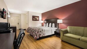 A hotel room with a bed, a desk, a television, a green sofa, and a wall-mounted picture. - Red Roof Inn & Suites Knoxville East (Knoxville)
