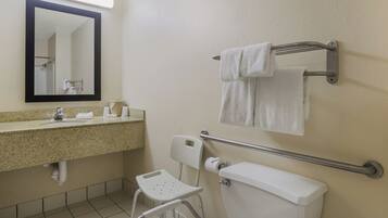 A bathroom with a sink, mirror, towel rack, toilet, and a wheelchair-accessible chair.