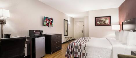 Una habitación de hotel con cama, escritorio, silla, microondas y televisor sobre un soporte.