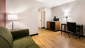 A hotel room with a green sofa, a desk with a computer, a coffee maker, and a lamp. - Red Roof Inn & Suites Knoxville East (Knoxville)