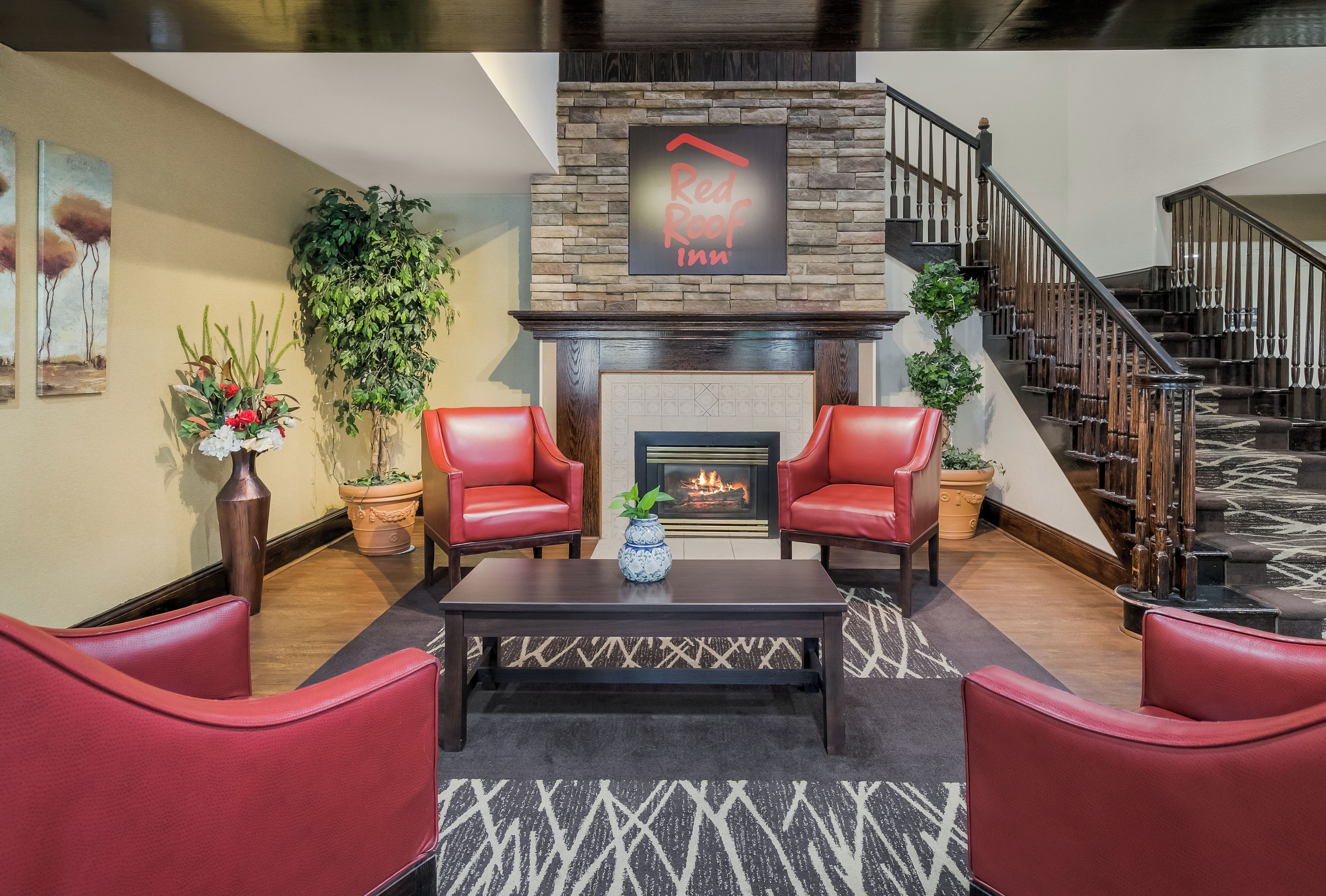 A modern living room with a fireplace, red leather chairs, a coffee table, and a staircase.