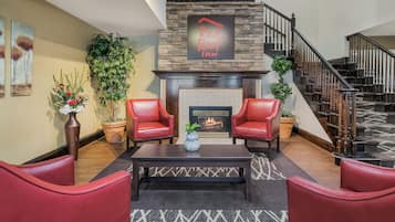 A modern living room with a fireplace, red leather chairs, a coffee table, and a staircase.