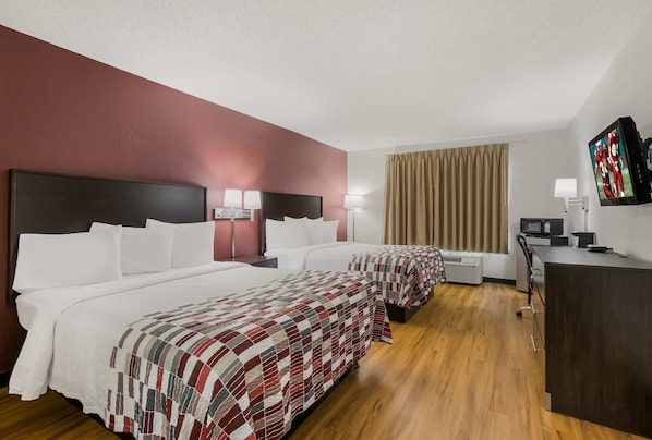A hotel room with two beds, a desk, a TV, and a window with curtains.