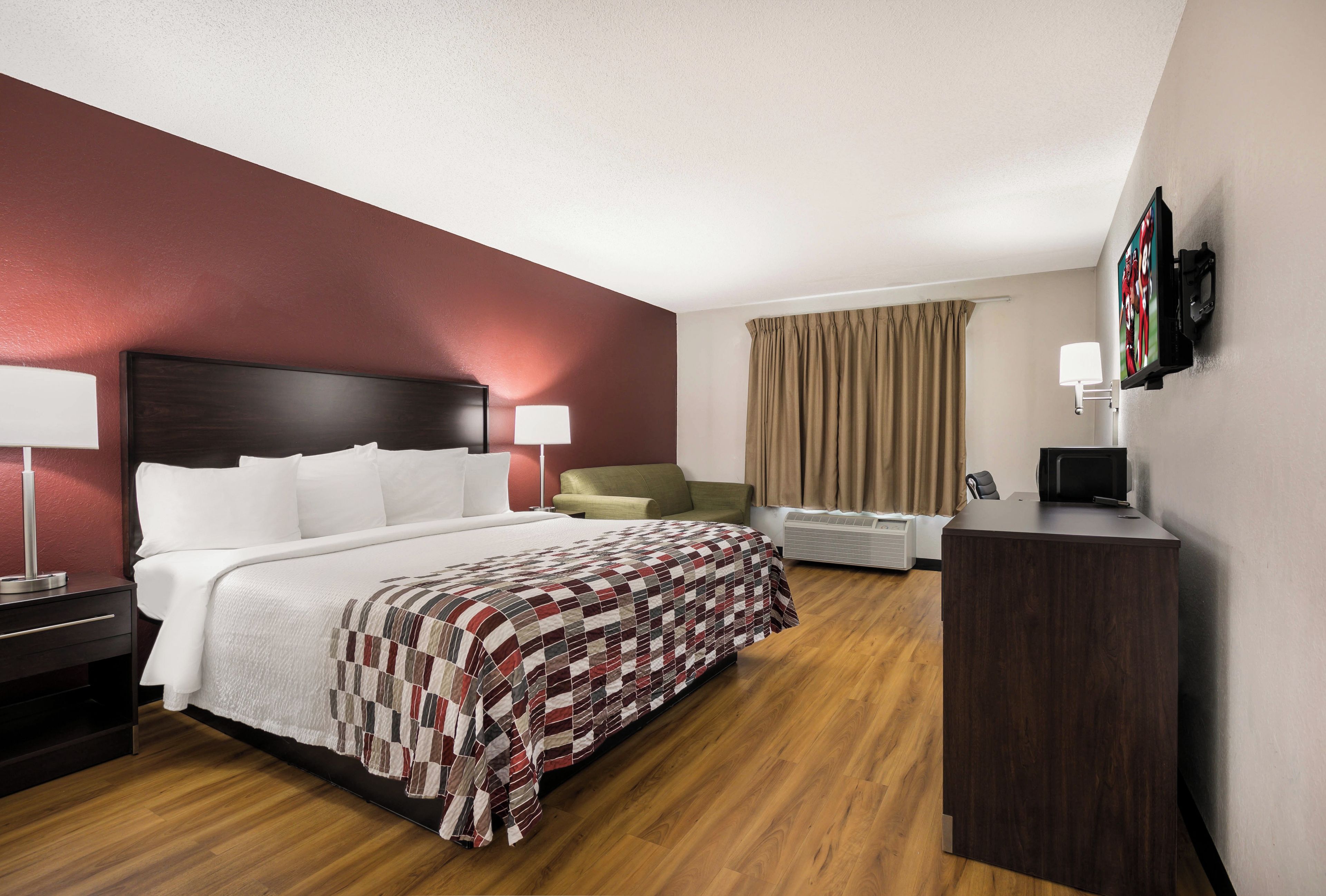 A hotel room with a large bed, a desk, a chair, a TV, and a window with curtains.
