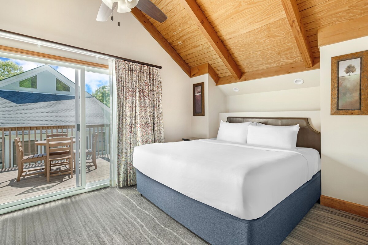 A bedroom with a large bed, a view of a deck, and a ceiling fan.