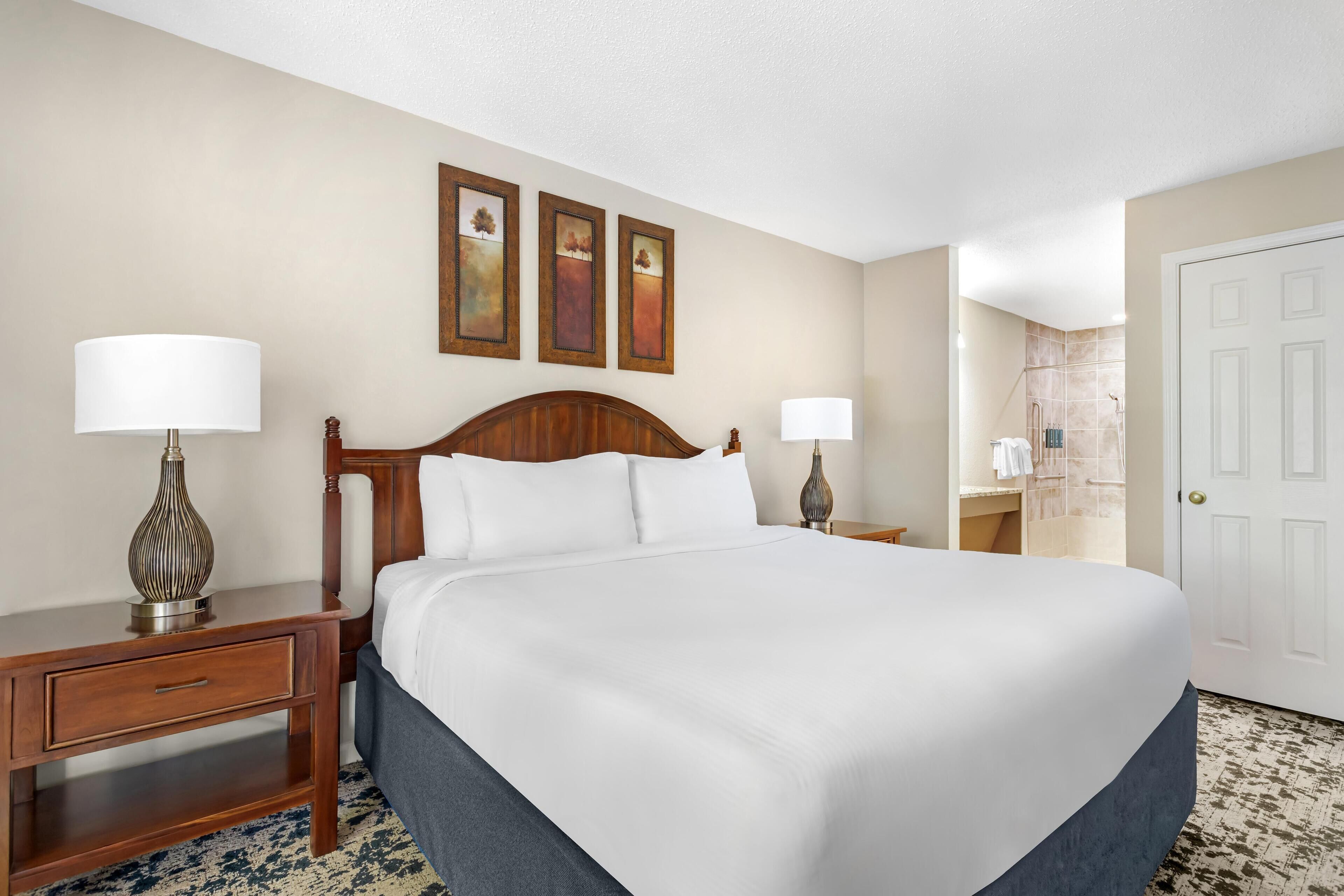 A hotel room with a large bed, two bedside tables, a wooden headboard, and three framed artworks on the wall.