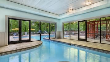 Una piscina interior con paredes de vidrio transparente, un jacuzzi y vistas de la vegetación circundante.
