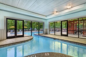 Una piscina interior con paredes de vidrio transparente, un jacuzzi y vistas de la vegetación circundante.