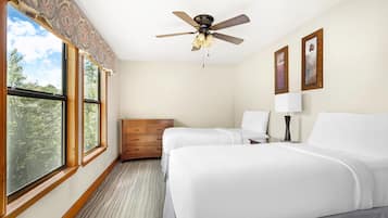 A hotel room with two beds, a ceiling fan, a dresser, and a window with a view of trees.