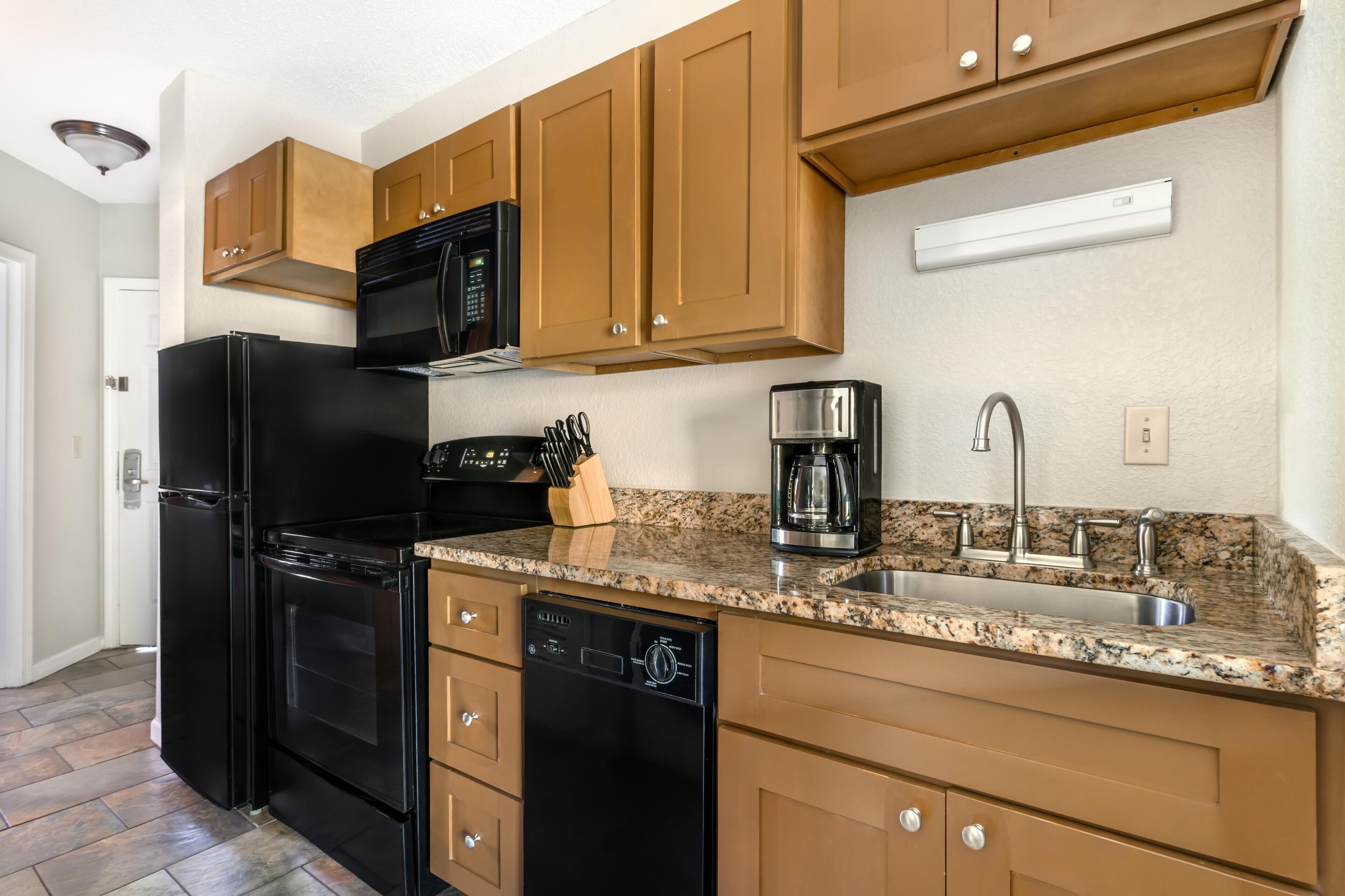 A kitchen with a black refrigerator, a coffee maker, and wooden cabinets.