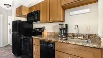 A kitchen with a black refrigerator, a coffee maker, and wooden cabinets.