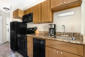 Una cocina con un refrigerador negro, cafetera y gabinetes de madera.