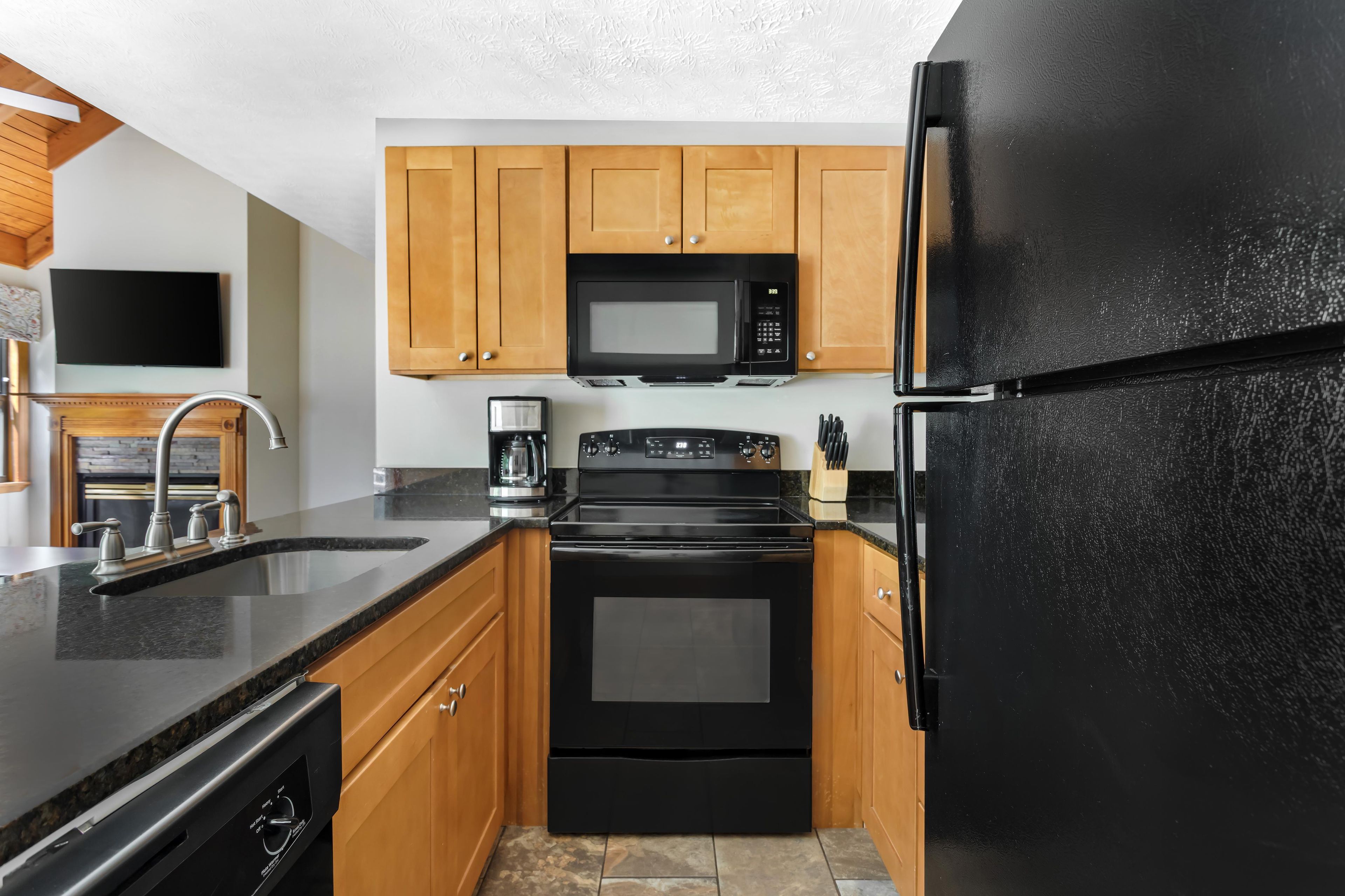 A modern kitchen with a black refrigerator, a microwave, a stove, and wooden cabinets.