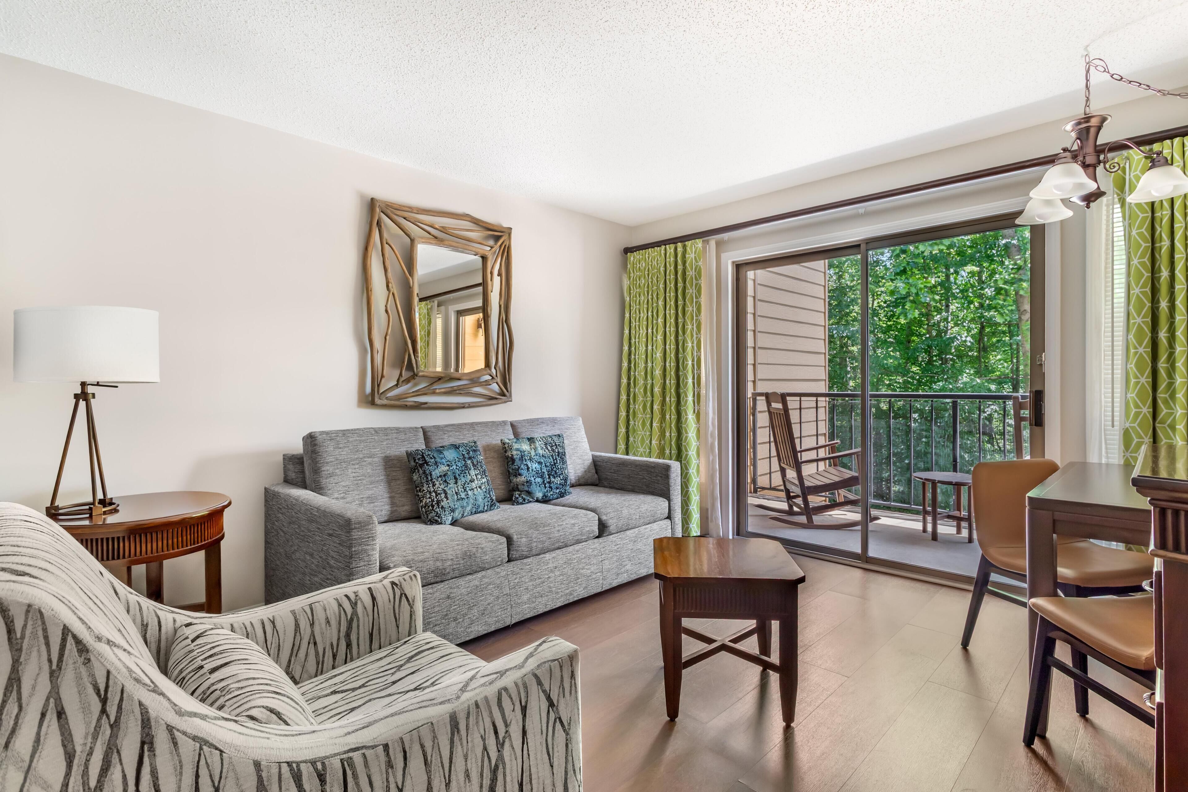 A modern living room with a grey sofa, patterned armchair, and a dining area with a table and chairs.