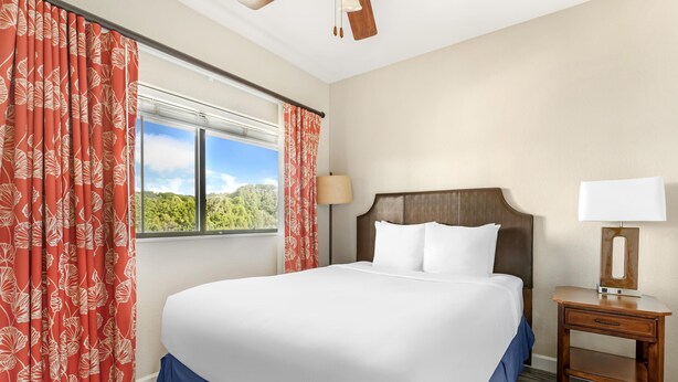 A hotel room with a large bed, a nightstand with a lamp, and a window with curtains.
