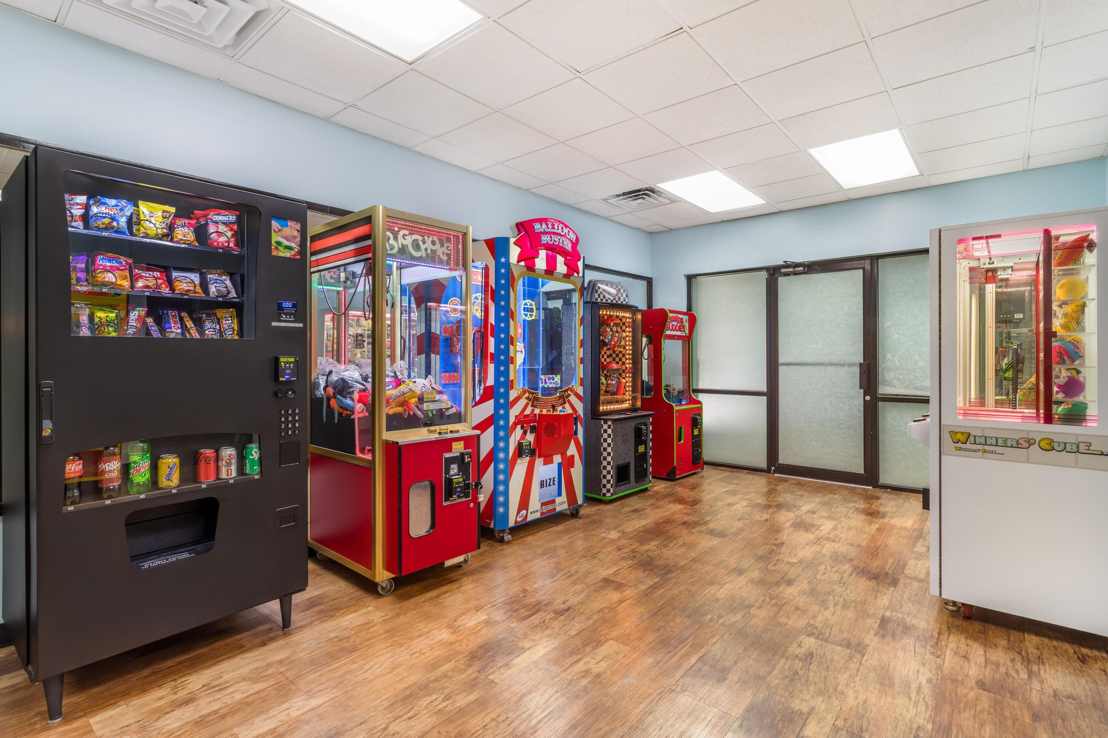 A row of arcade machines and vending machines in a room with wooden flooring and a tiled ceiling.
