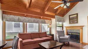 A living room with a wooden ceiling, a fireplace, a sofa, a table, and a chair.