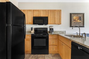 Una cocina con electrodomésticos negros, gabinetes de madera, encimera de granito y pileta de acero inoxidable.