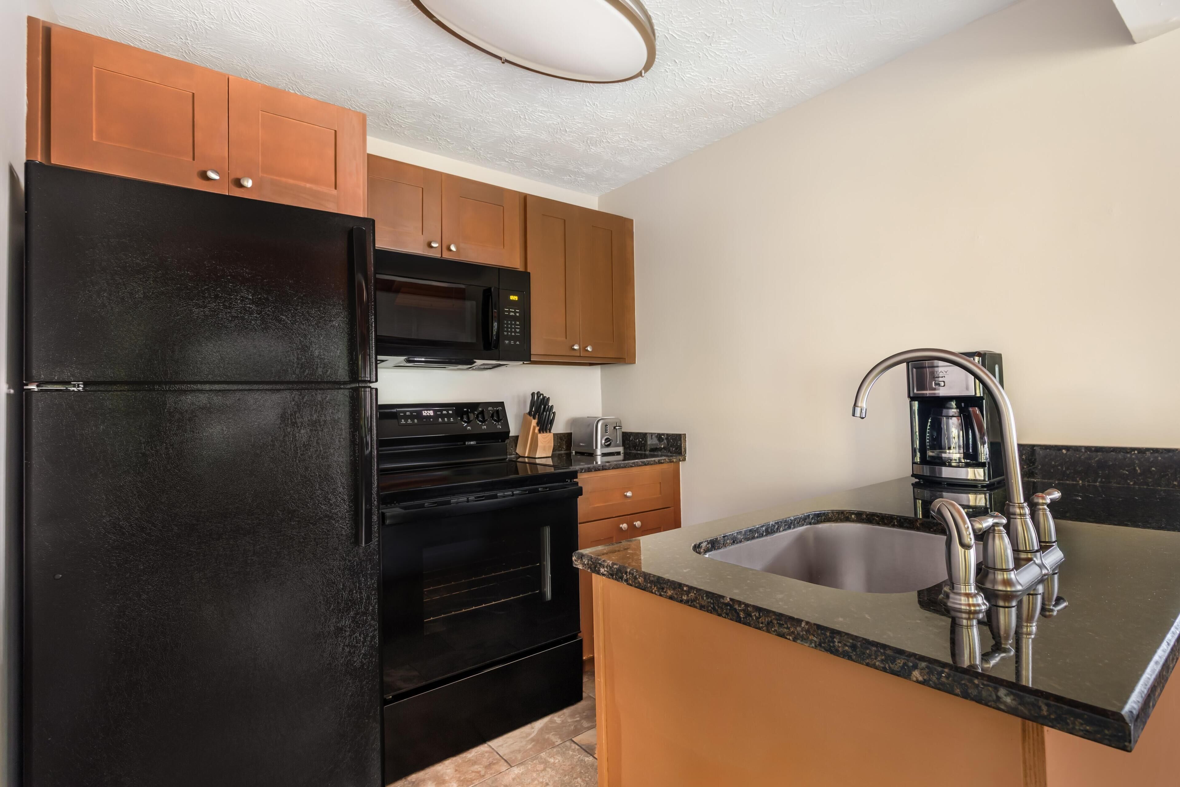 A kitchen with a black refrigerator, stainless steel sink, and wooden cabinets.