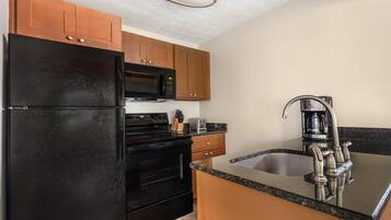 A kitchen with a black refrigerator, stainless steel sink, and wooden cabinets.