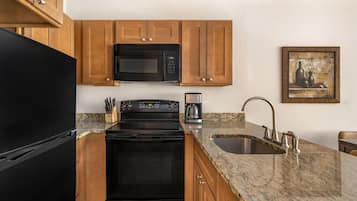 A kitchen with wooden cabinets, a black refrigerator, a microwave, a stove, a coffee maker, and a sink.