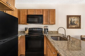 Una cocina con armarios de madera, un refrigerador negro, un microondas, una estufa, una cafetera y un lavabo.