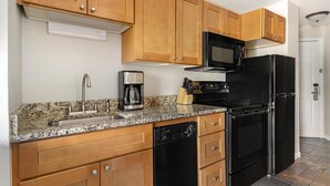 A kitchen with wooden cabinets, a stainless steel sink, a coffee maker, a microwave, and a black refrigerator.