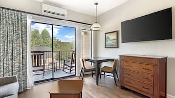 A room with a sliding glass door leading to an outdoor balcony, a dining table with chairs, a wooden dresser, and a flat-screen TV mounted on the wall.