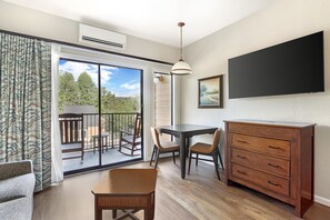 Una habitación con puerta corrediza de vidrio que da a un balcón exterior, una mesa de comedor con sillas, un aparador de madera y un televisor de pantalla plana montado en la pared.