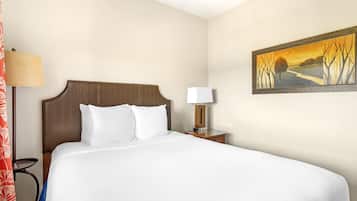Quarto de hotel com uma cama grande, mesa de cabeceira com abajur e um quadro na parede.