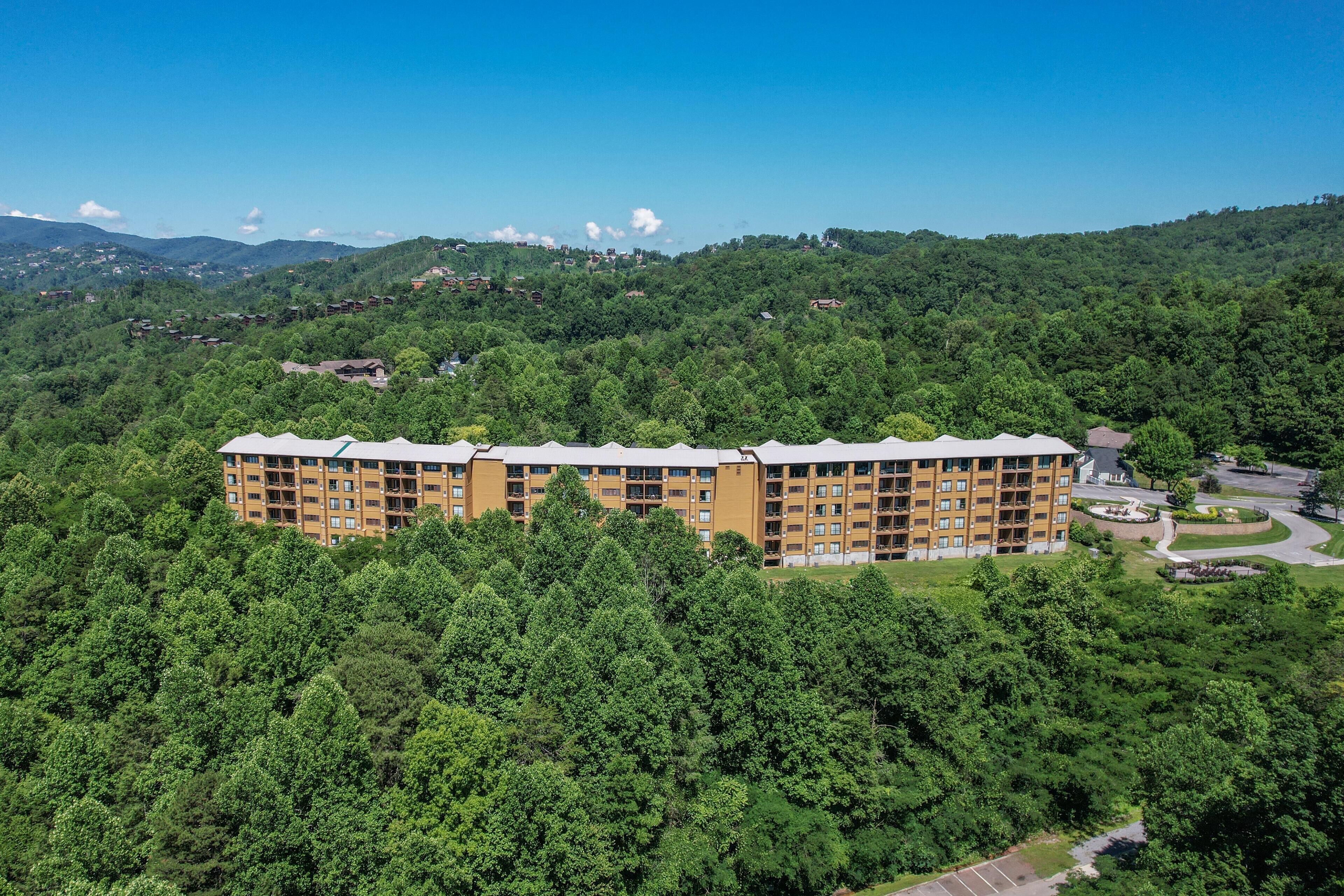 A multi-story hotel with a flat roof, surrounded by dense forest, and a clear sky.