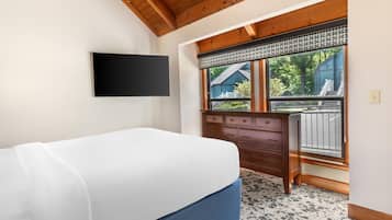 A bedroom with a bed, a dresser, a television mounted on the wall, and a window with a view of the outside.