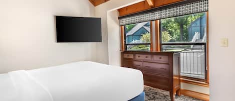 Ein Schlafzimmer mit einem Bett, einer Kommode, einem an der Wand befestigten Fernseher und einem Fenster mit Blick ins Freie.