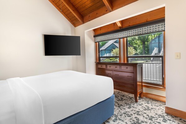 Un dormitorio con cama, cómoda, televisor montado en la pared y ventana con vistas al exterior.