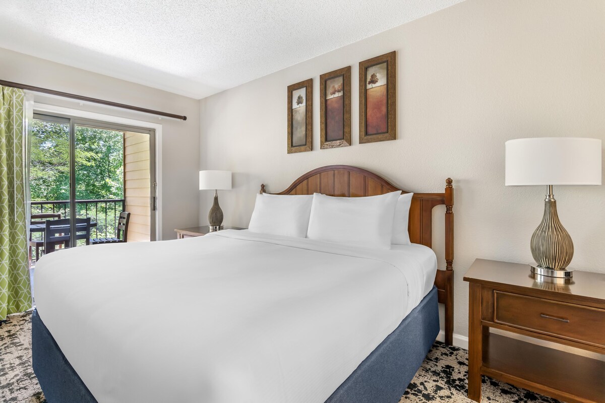 A hotel room with a large bed, two bedside tables, a window with a view, and a balcony.