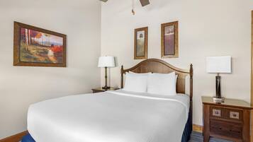 A hotel room with a large bed, two bedside tables, a ceiling fan, and three framed artworks on the wall.
