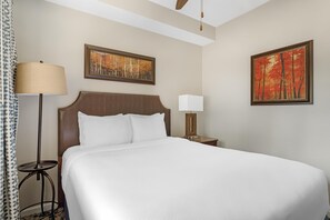 Una habitación de hotel con una cama, dos mesitas de noche, una lámpara de pie y dos cuadros en las paredes.