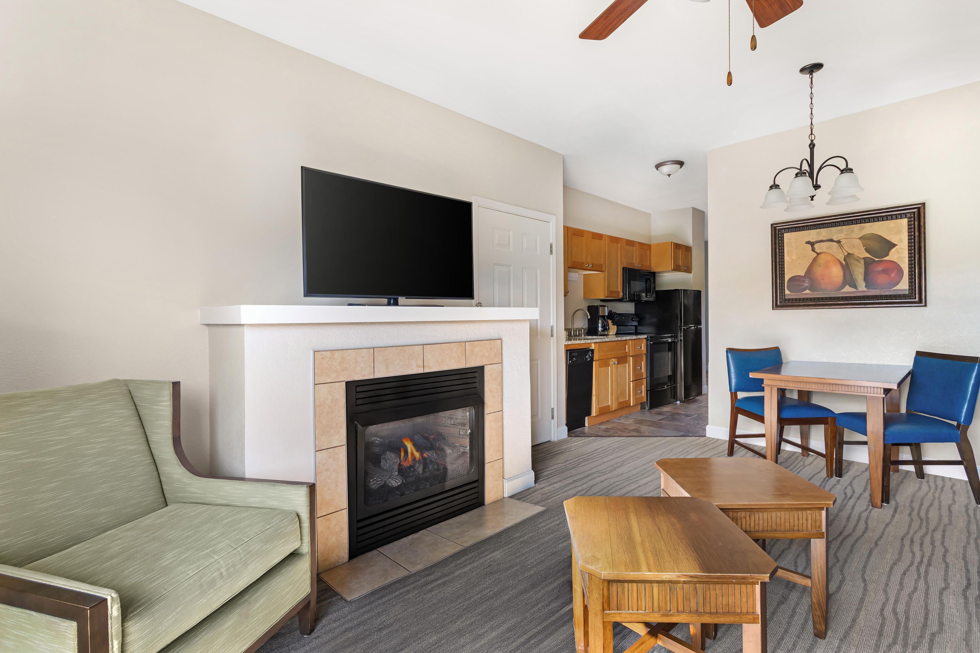 Una sala de estar con una televisión de pantalla plana, chimenea, sofá, mesa de comedor con sillas y una cocina al fondo.