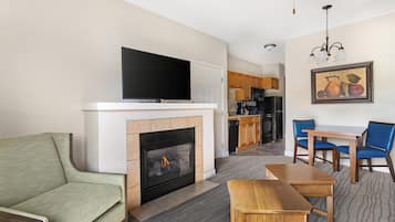 Una sala de estar con una televisión de pantalla plana, chimenea, sofá, mesa de comedor con sillas y una cocina al fondo.
