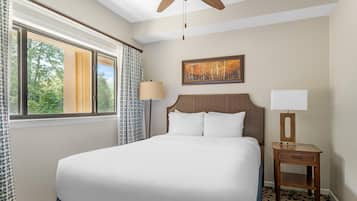 Quarto de hotel com uma cama grande, uma mesa de cabeceira com abajur, um quadro na parede e uma janela com cortinas.