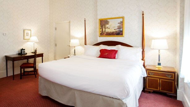 A hotel room with a large bed, two bedside tables with lamps, a desk with a chair, and a painting on the wall.