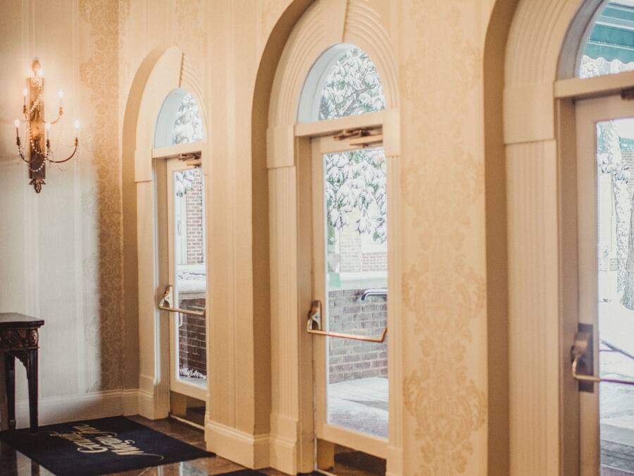 A hallway with arched doorways, a chandelier, and doormats with text.