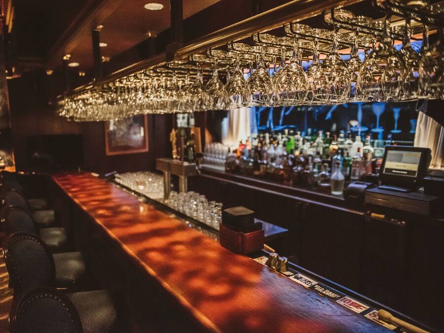 A bar area with a long counter, multiple glasses hanging above, and a variety of bottles and glasses on the shelves.