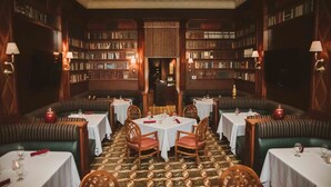 A library-style restaurant with multiple tables and booths, surrounded by bookshelves.
