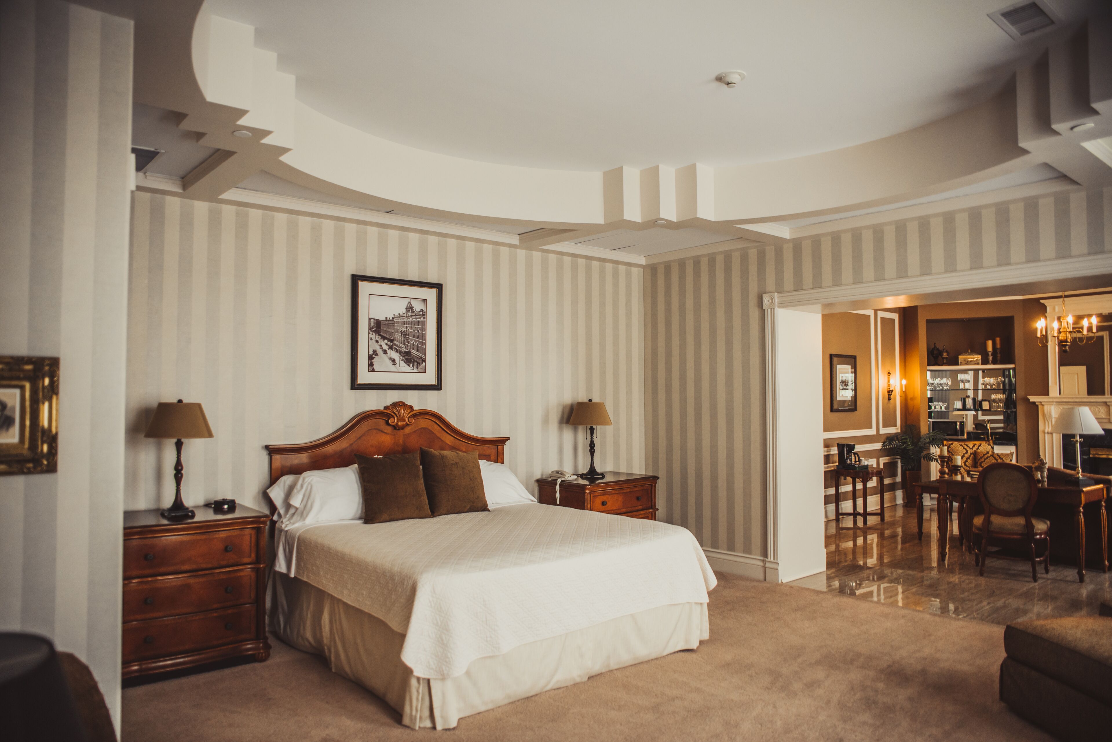 Een ruime slaapkamer met een groot bed, houten hoofdbord en uitzicht op een eetgedeelte.