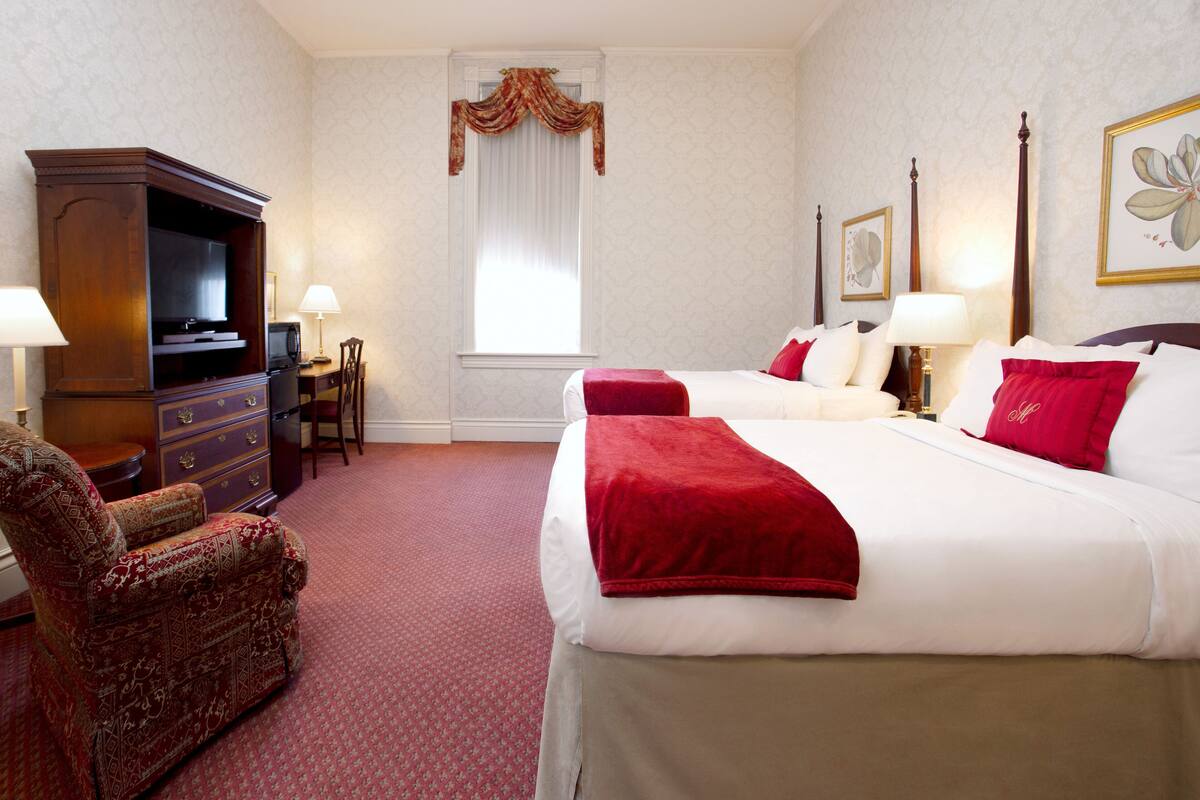 A hotel room with two beds, a TV, a desk, and a chair.